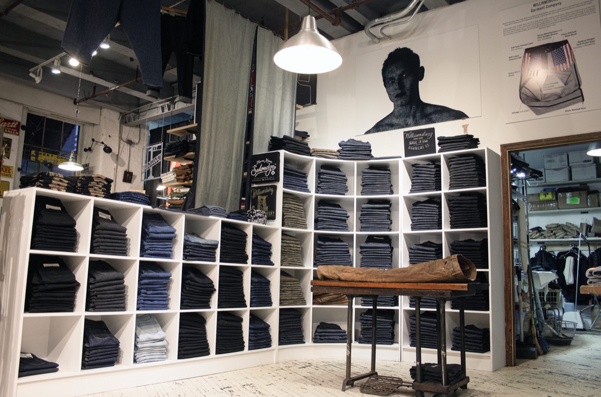 The Williamsburg Garment Company shop display, shelves of folded jeans beneath a portrait of Maurice Malone